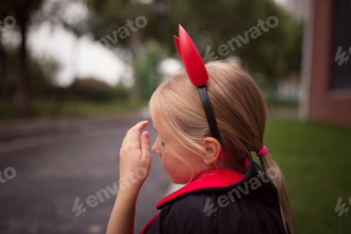 Preview: Little Girl in costume of devil with red horns in park. Happy Halloween concept