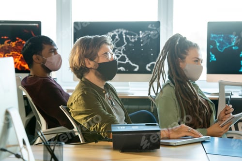 Preview: Group of students in protective masks sitting by desks and listening to coach