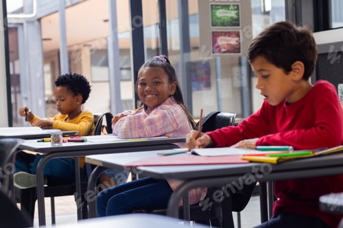 Preview: Three children are focused on coloring at desks in a school classroom setting