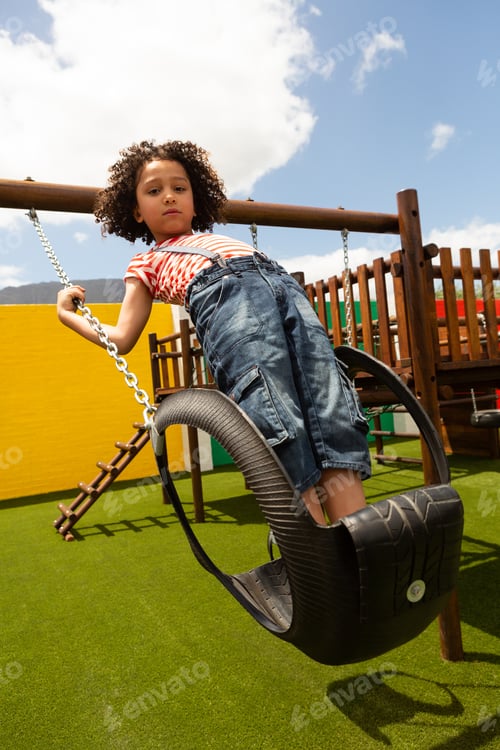 Preview: Schoolgirl looking at the camera while playing on a swing at school playground