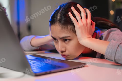 Preview: Stressful Asian business woman sitting on the chair and looking on the laptop screen.