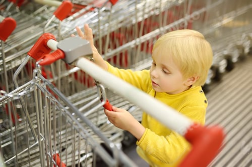 Preview: A cute blonde boy plays with shopping carts at the entrance to the supermarket
