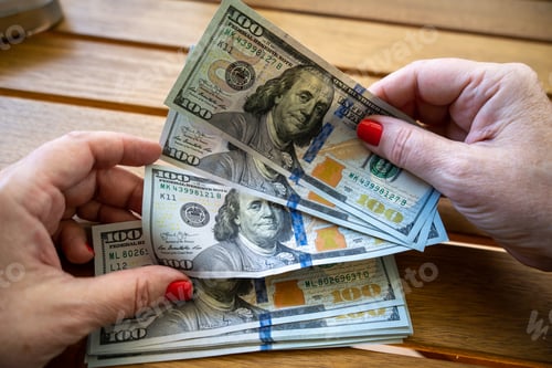 Preview: Closeu of a person counting cash dollar bills on a wooden surface