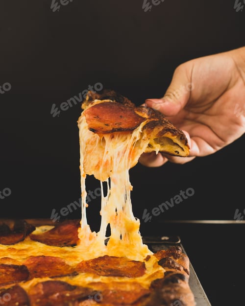 Preview: Hand holding a piece of freshly-baked pepperoni pizza, with a slice being lifted up from it