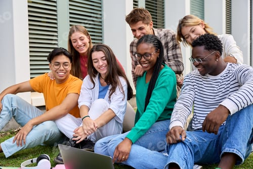 Preview: Group of young multiracial university students looking smiling at laptop screen sitting on campus