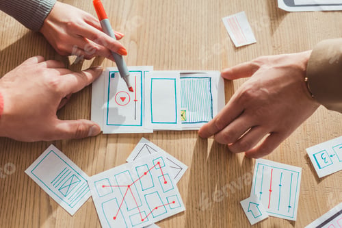 Preview: Cropped view of creative designers developing user experience design with layouts on table