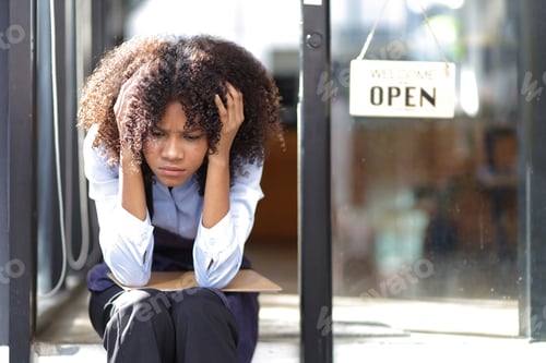 Preview: Young African woman running a small start-up business sits at the entrance looking absent-minded.
