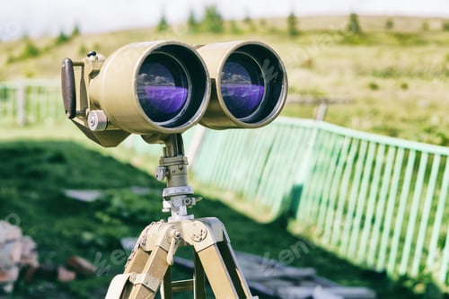 Preview: Old khaki green military binoculars. Sky and clouds reflection in the lenth glass.