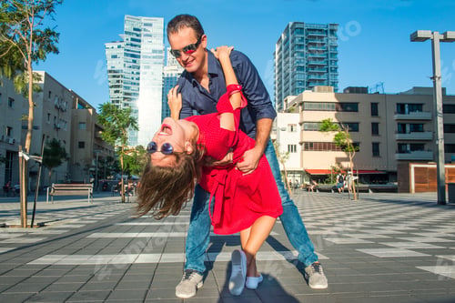 Preview: Emotional young happy couple in bright clothes and sunglasses having fun on the city square