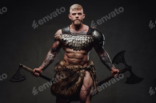 Preview: Brutal tattooed warrior wearing light armour and fur holding axes in dark studio
