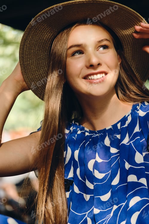 Preview: Close up beautiful smiling girl in blue dress and hat happily sitting in city park