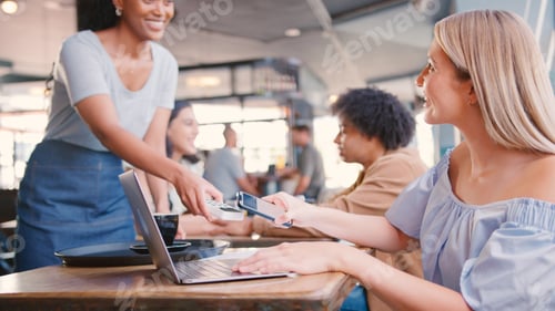 Preview: Woman Using Laptop In Coffee Shop Paying Bill With Contactless Mobile Phone Payment