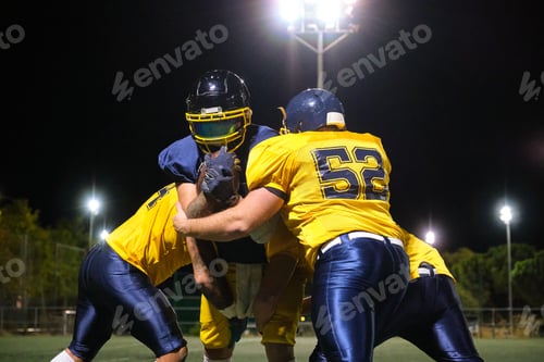 Preview: American football players tackling during night game on field