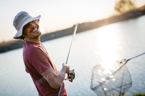 Preview: Young man fishing on a lake at sunset and enjoying hobby