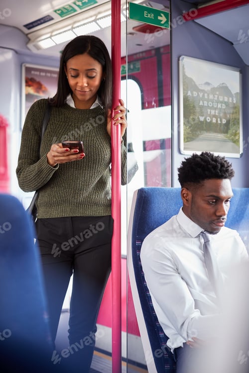 Preview: Female Passenger Standing By Doors In Train Looking At Mobile Phone