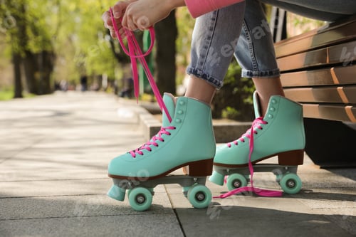 Preview: Woman lacing roller skates while sitting on bench outdoors, closeup