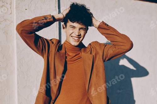 Preview: Joyful young man with curly hair smiling against a light wall background