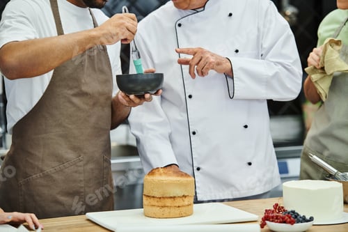 Preview: cropped view of young african american man brushing cake with syrup next to chef and his friends
