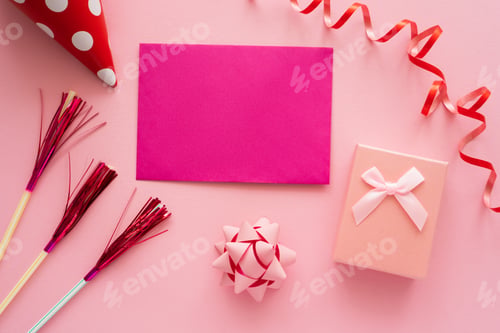 Preview: Top view of pink greeting card near gift box and serpentine on pink background
