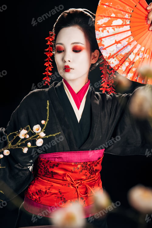 Preview: selective focus of beautiful geisha in black kimono with red flowers in hair holding hand fan and