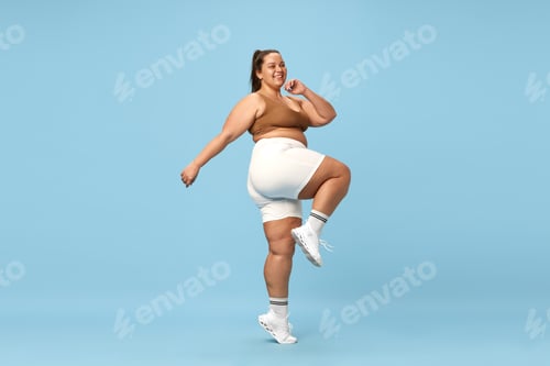 Preview: Young, positive, smiling overweight woman sportswear doing cardio exercises on blue background
