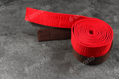 Preview: Red and brown karate belts on gray textured background, space for text