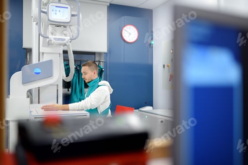 Preview: Young man having x-ray shot of broken hand in x-ray room in modern clinic.