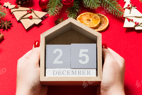 Preview: Top view of female hands holding calendar on red background. The twenty fifth of December