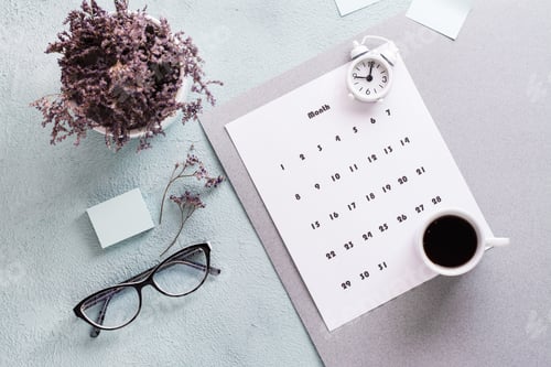 Preview: Monthly calendar sheet, coffee cup, alarm clock, glasses and a bouquet of flowers on the table.