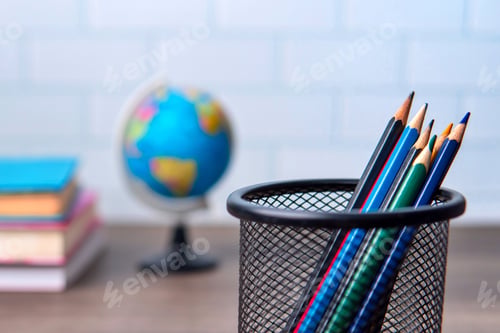Preview: A close-up shot of a pencil holder filled with colored pencils, a globe and a stack of books.