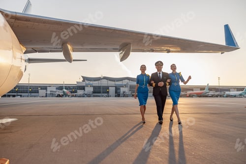 Preview: Full length shot of excited male pilot walking together with two female flight attendants