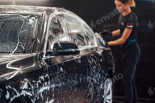 Preview: Modern black automobile get cleaned by woman inside of car wash station