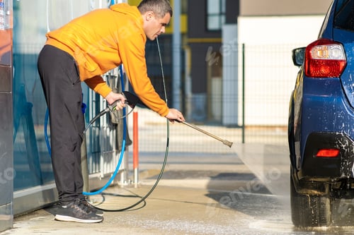 Preview: Young driver man washing his car with contactless high pressure water jet in self service car wash.