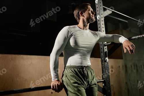 Preview: Professional Sportsman in White Long Sleeve Posing next to High Bars in Gym