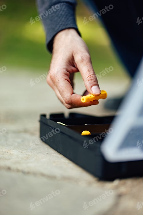 Preview: Hand Holding Yellow Object with Black Box Outdoors in Bright Sunlight