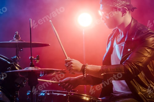 Preview: side view of young male musician in leather jacket playing drums during rock concert on stage