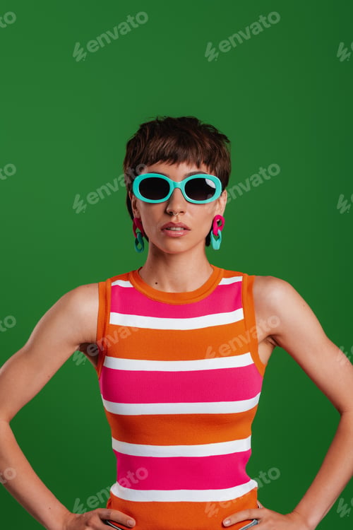 Preview: Fashionable young woman in trendy glasses looking at camera while standing against green background