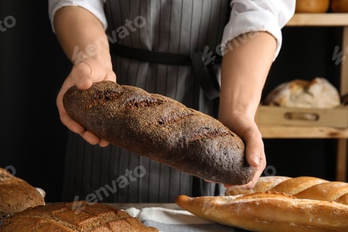 Preview: Baker holding loaf of bread over table indoors, closeup