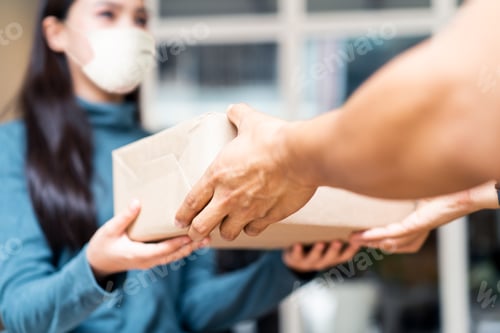Preview: Young Asian cute girl wearing face mask recieve two boxes from postman at the door.