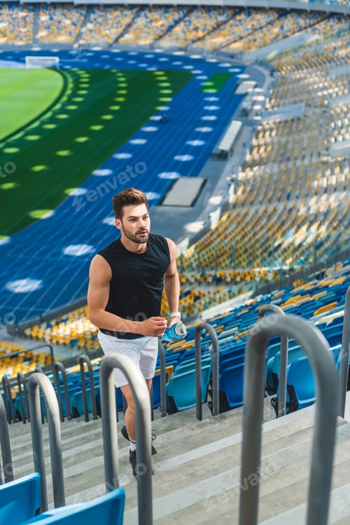 Preview: high angle view of handsome young man jogging upstairs at sports stadium