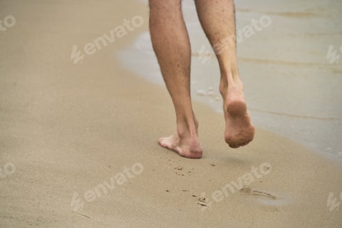 Preview: Closeup of feet of a man walking on a sandy shore