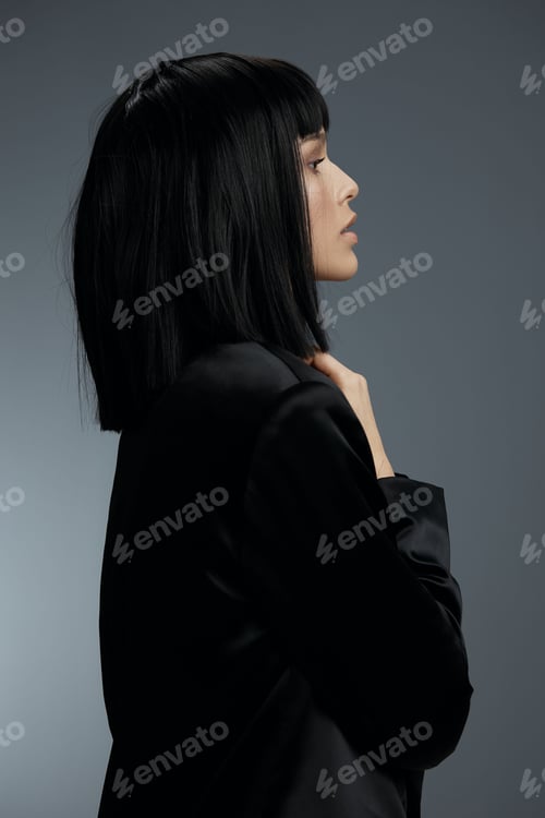 Preview: Blackhaired woman in black jacket standing against gray background, hands on hips, looking to the
