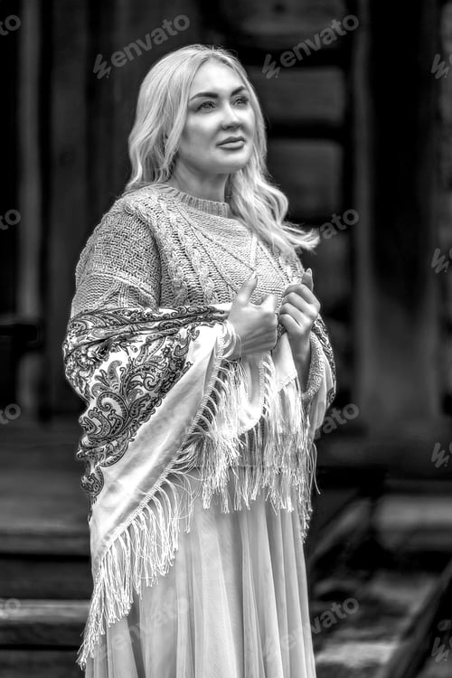 Preview: A blonde Russian woman in a national Russian headscarf on the porch of a log village house. Vintage