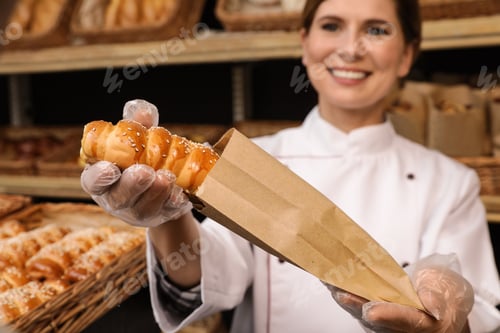 Preview: Baker putting fresh bun into paper bag in store