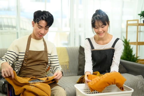 Preview: Cheerful young couple folding laundry together in a cozy living room