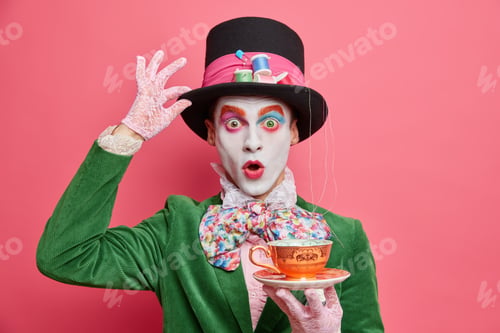 Preview: Surprised male hatter wears gentlemans clothes holds cup of hot tea pretends to come from wonderland