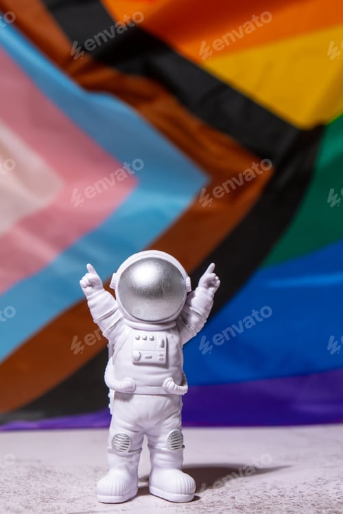 Preview: Toy astronaut on Rainbow LGBTQIA flag made from silk material background. Happy pride month. Symbol