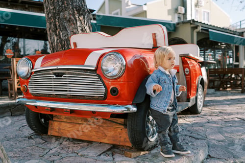 Preview: Little girl stands leaning on a red retro car