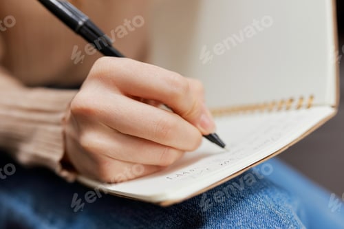 Preview: Closeup shot of hand blonde student lady with copybook sitting in sofa couch at modern living room