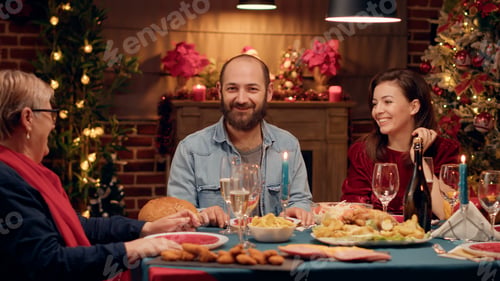 Preview: Happy man talking with senior woman and smiling at camera while enjoying Christmas dinner